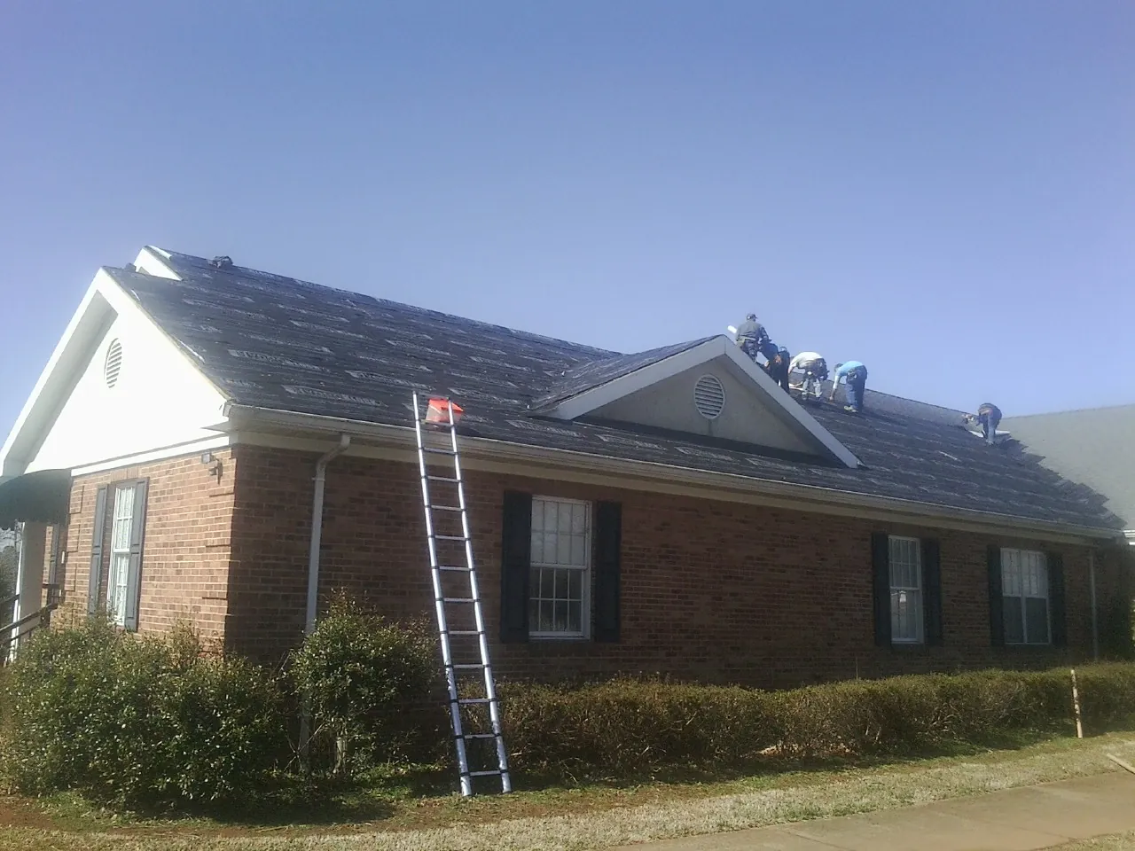 Crew tearing shingles off a brick ranch roof with a ladder set — Emergency Roof Repair work by our crew in Pendleton
