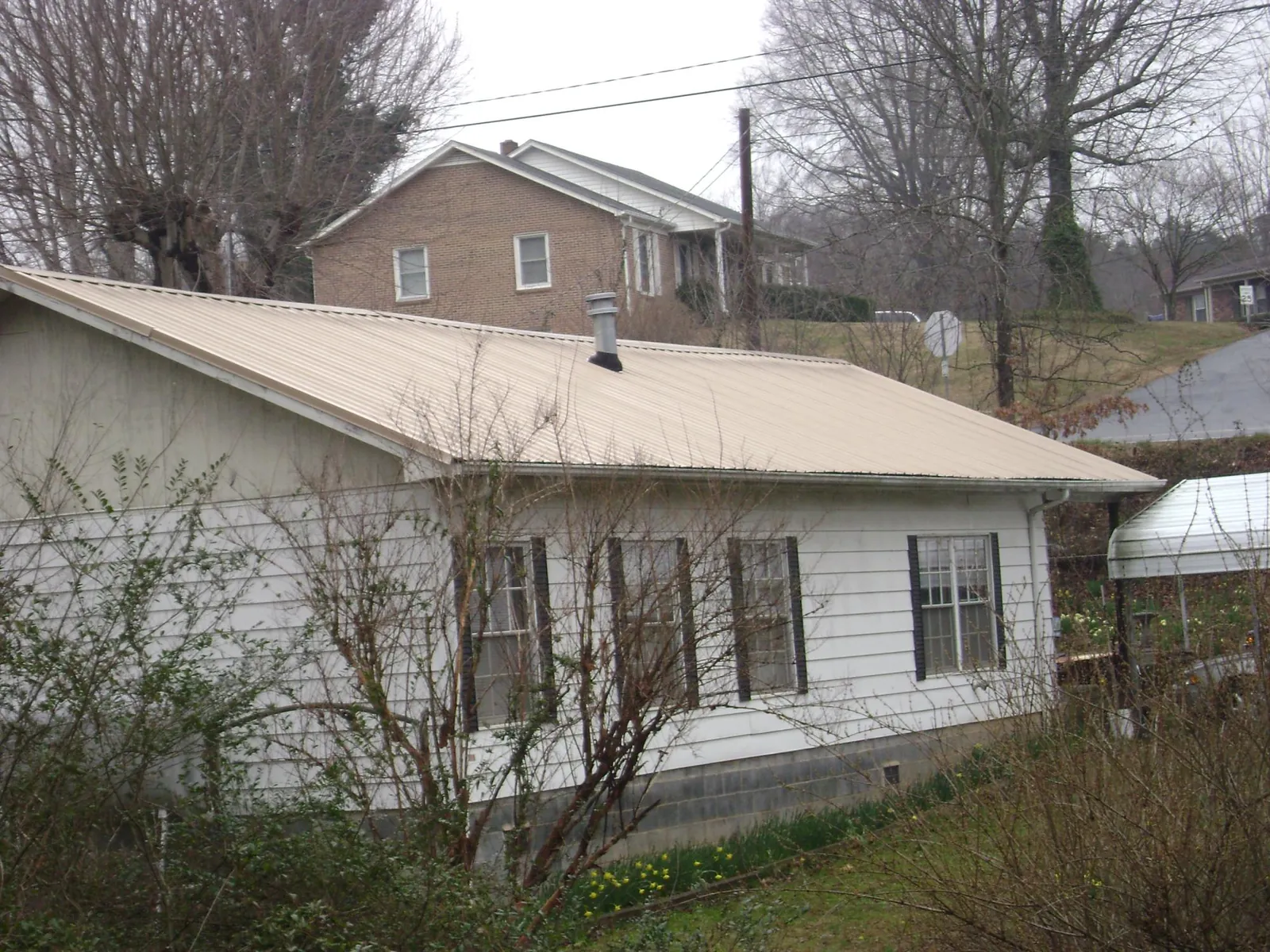 Tan metal roof on a white sided house set into a hillside — Commercial Roofing by Roofing Brothers in Pendleton